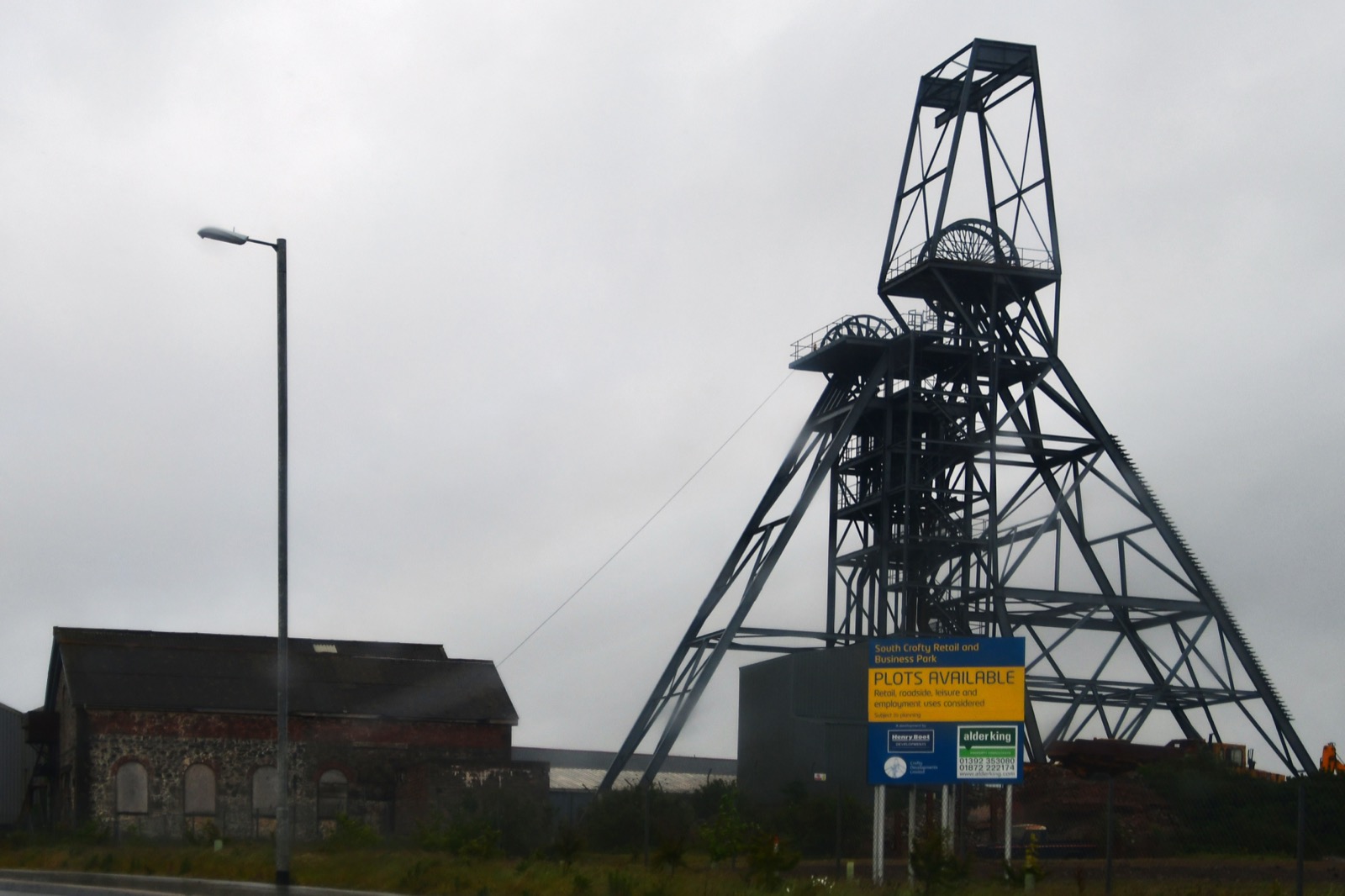 A steel headframe and old brick mine buildings at South Crofty under grey cloud