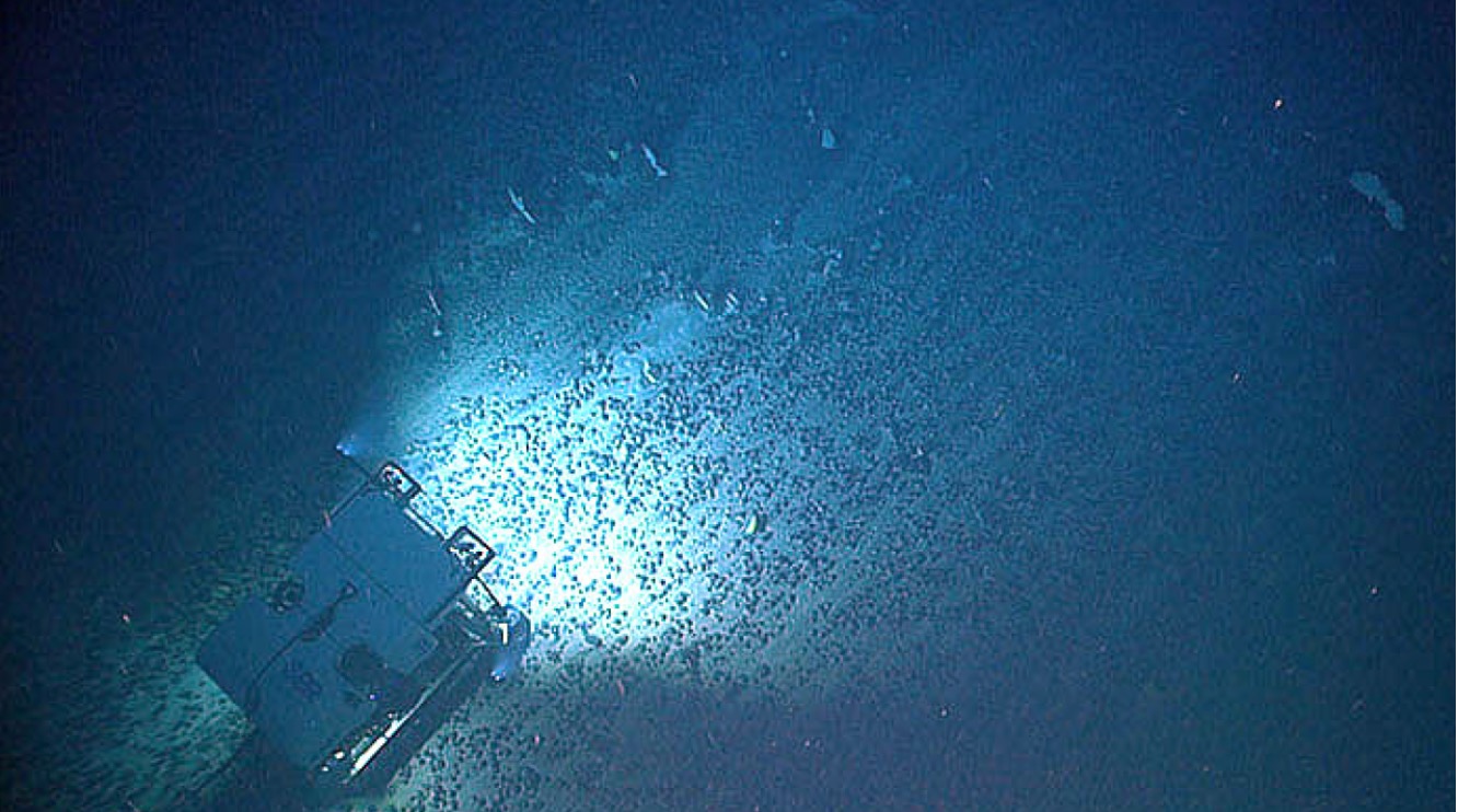 A remotely operated vehicle lit up over a field of dark nodules on the deep seafloor